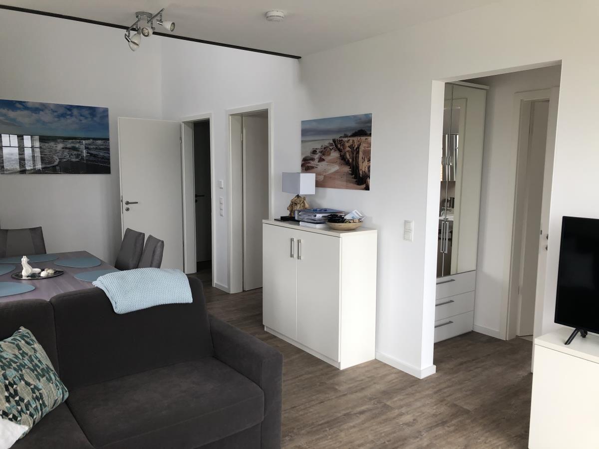 Living room with sofa, dining table, and TV. White walls and wooden floor.