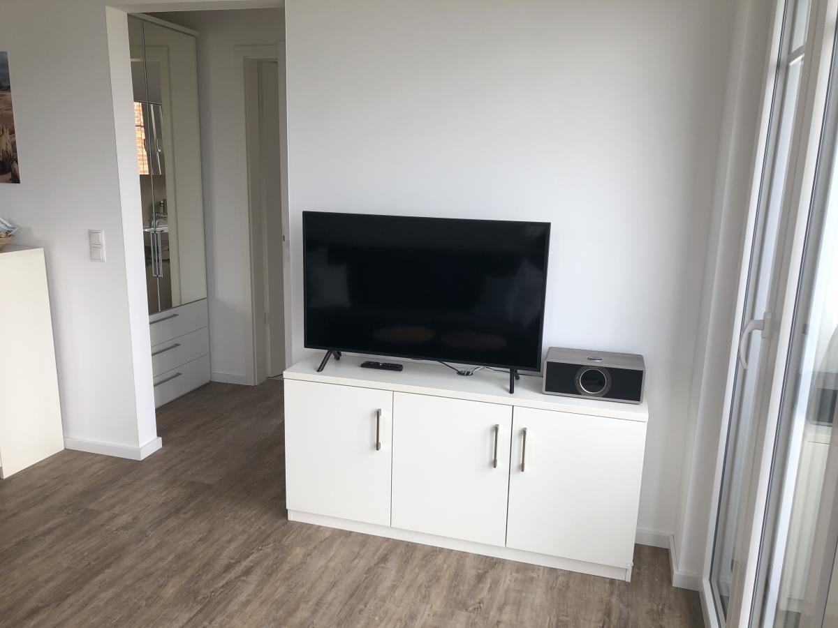 TV on white cabinet, speaker beside, window nearby