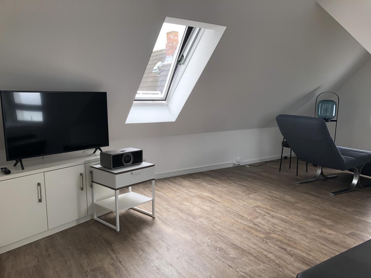 Attic room with TV, window, and seating area.