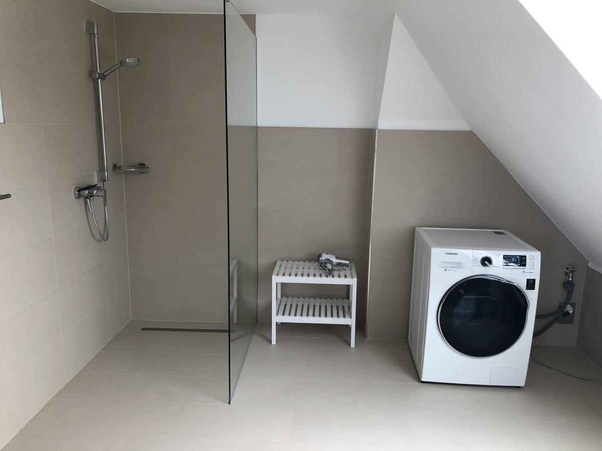 Shower with glass partition, washing machine, and small white stool.