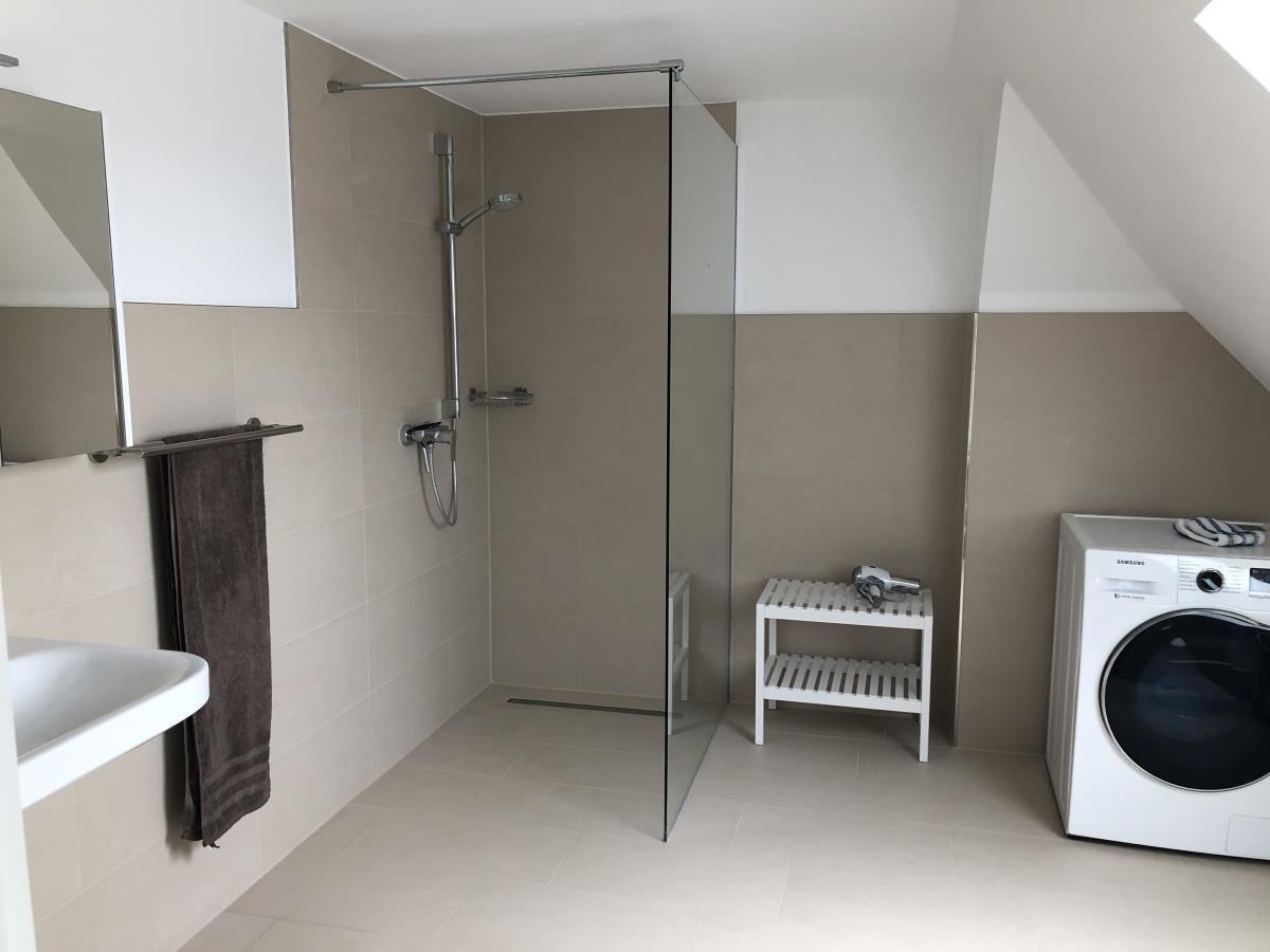 Bathroom with shower, washing machine, and towel rack.