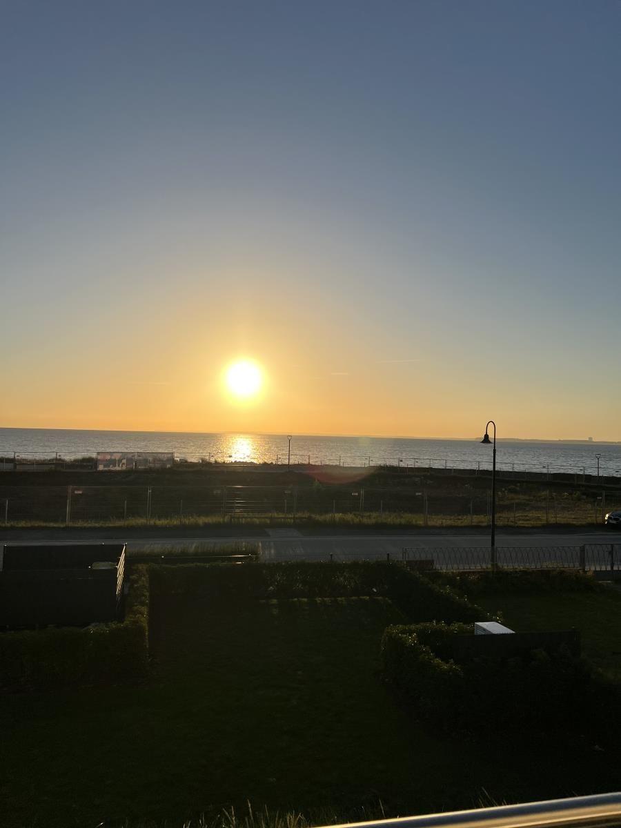 Sunset over the sea with road and green areas in the foreground.