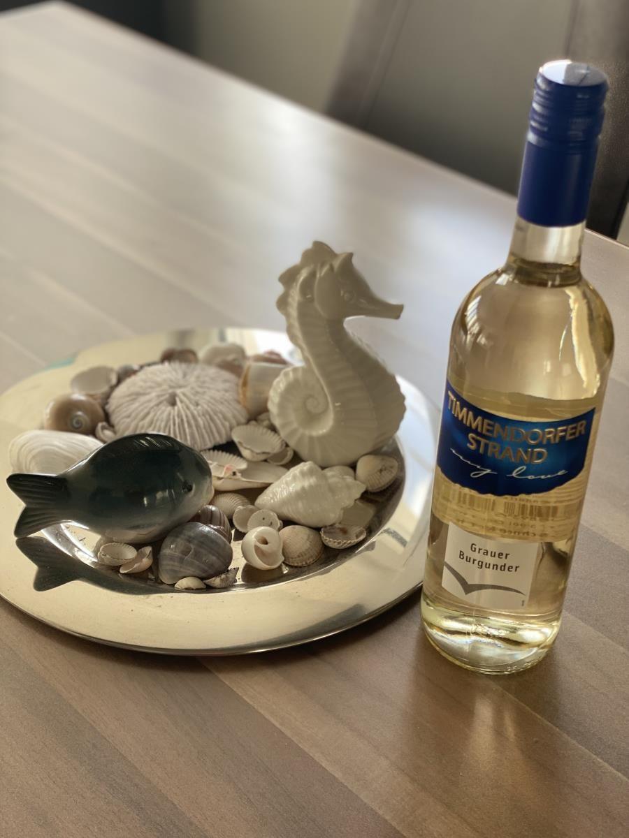 A bottle of white wine next to a dish with shells and a seahorse.