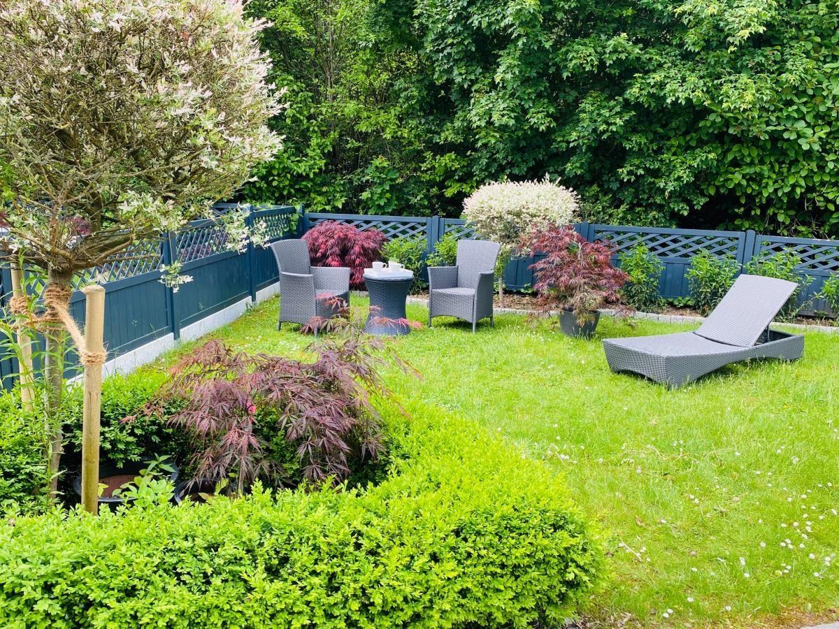 Garten mit Liegestuhl, Sitzgruppe und Pflanzen hinter blauem Zaun.