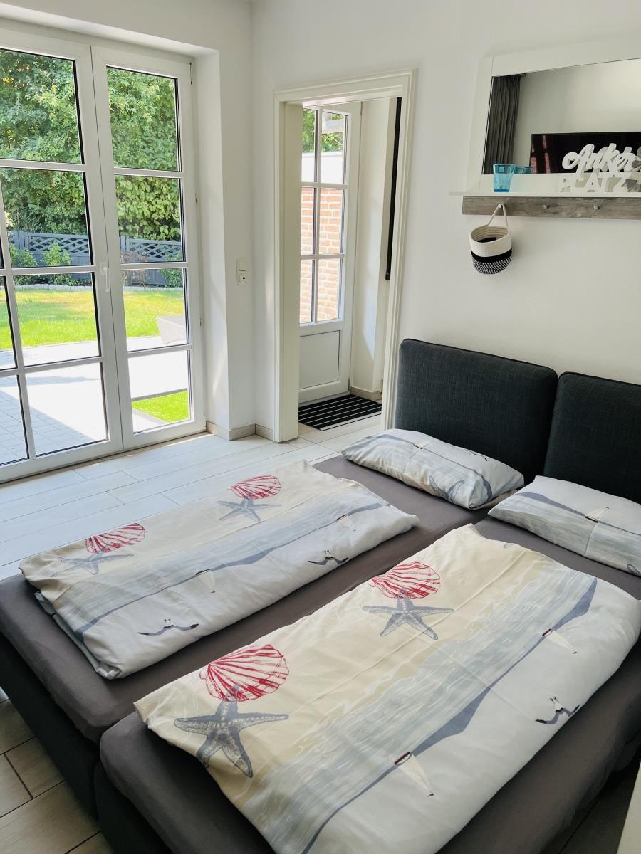 Schlafzimmer mit Doppelbett, Fenster zur Terrasse und Spiegel an der Wand.