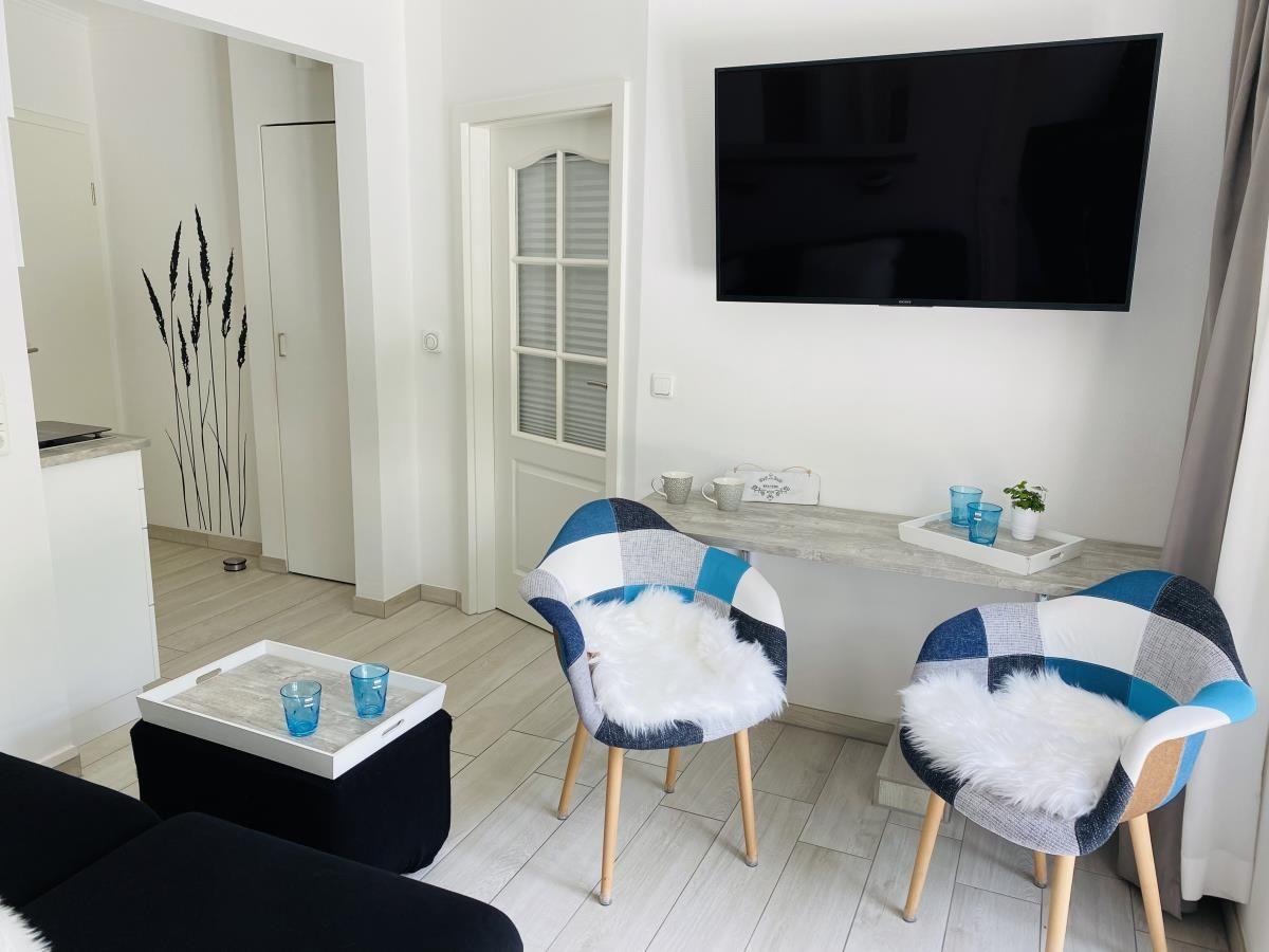 Wohnzimmer mit TV, zwei Stühlen und Tisch. Hintergrund: Tür und Wanddekoration.