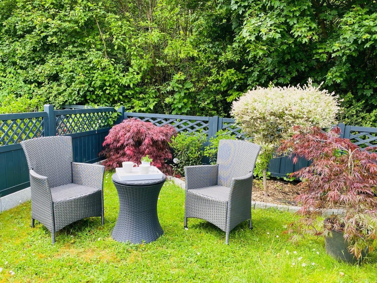 Garten mit zwei Stühlen und Tisch, umgeben von Pflanzen und Zaun.