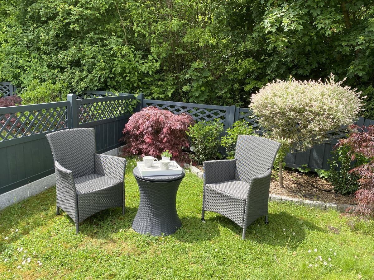Garten mit zwei Stühlen und Tisch, umgeben von Pflanzen und Zaun.