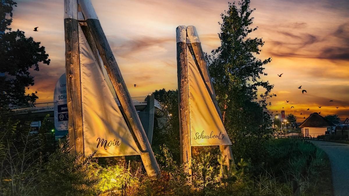 Zwei hölzerne Schilder mit den Aufschriften Moin und Scharbeutz stehen im Sonnenuntergang.