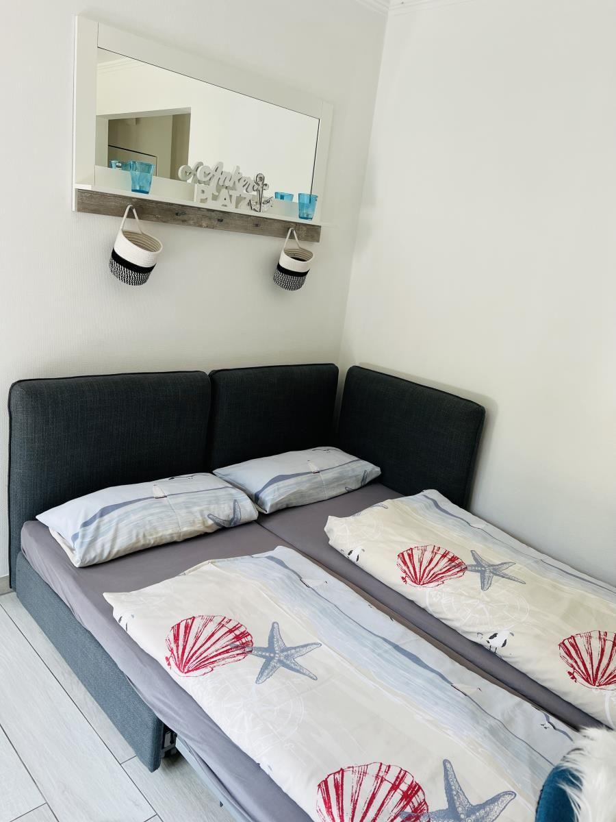 Zimmer mit Bett, Spiegel und Wandregal mit Körben.