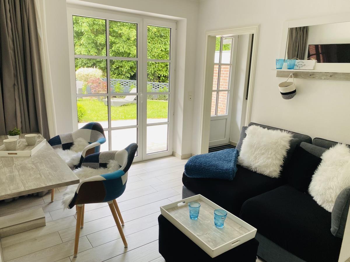 Wohnzimmer mit Sofa, Tisch und Stühlen. Durchgang zur Terrasse mit Gartenblick.