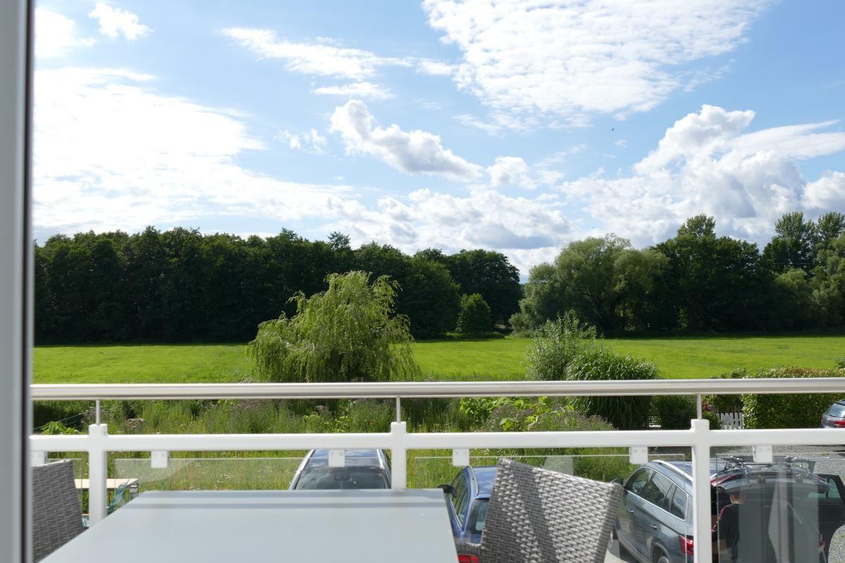 Balcony with table and chairs offers view of green field and forest.