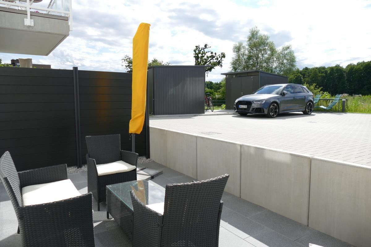 Terrace with seating group and yellow umbrella. Backyard with carport and car.