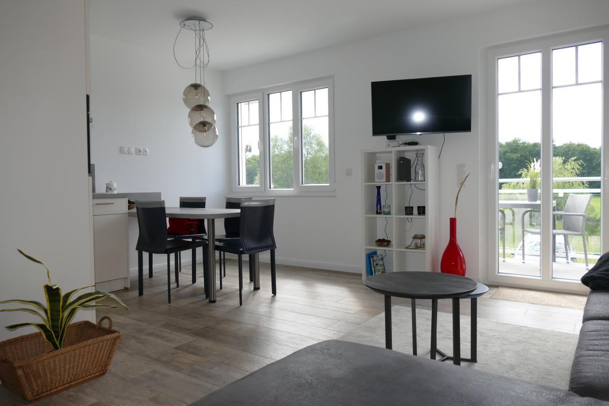 Living and dining area with TV, table, chairs, and balcony access.