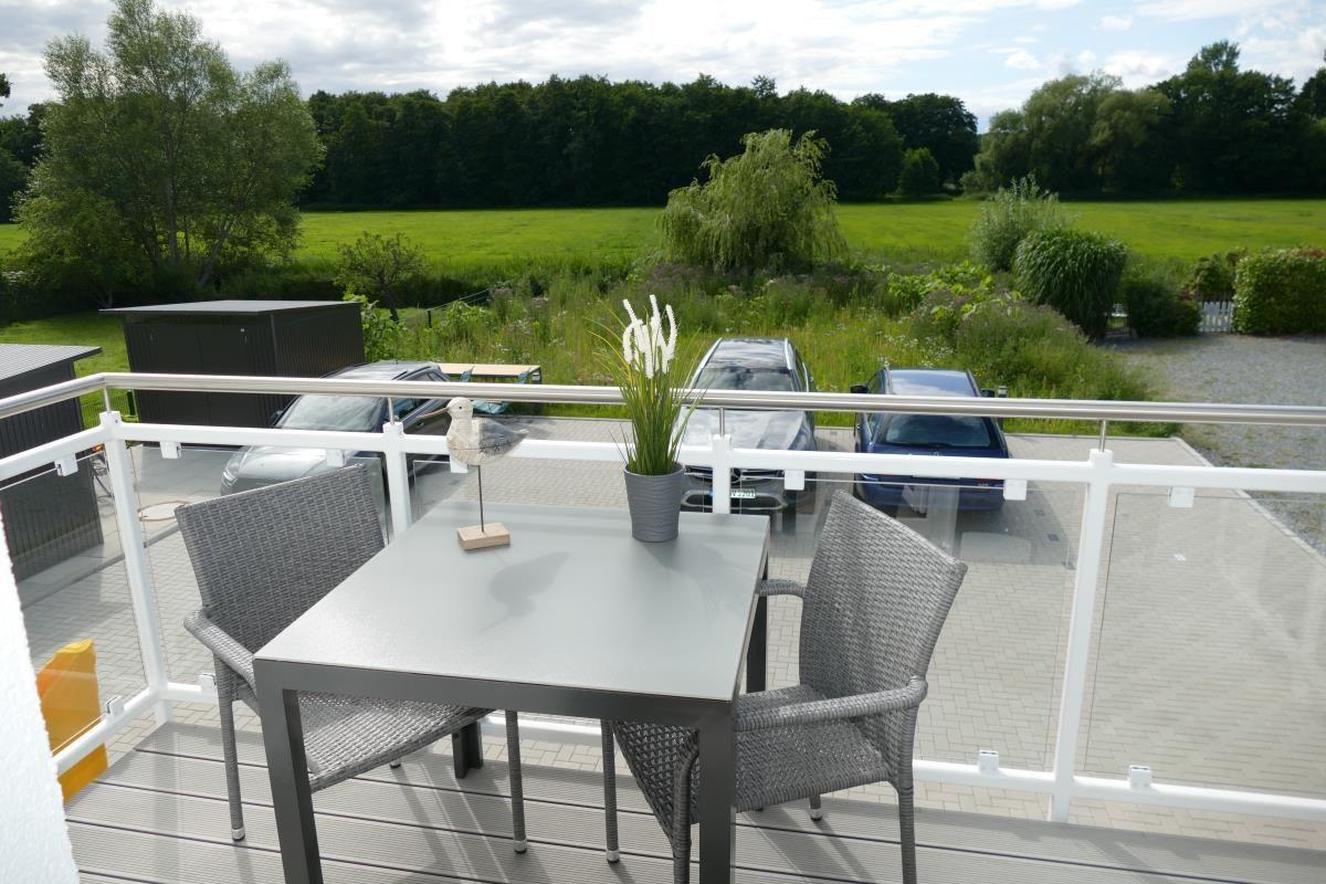 Terrace with table and chairs, view of green field and trees.