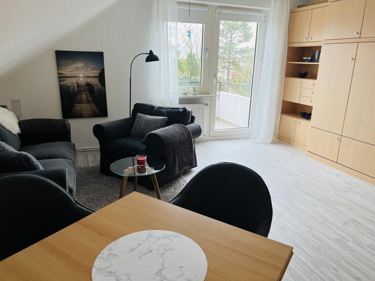 Wohnzimmer mit Sofa, Sessel, Tisch und Balkonzugang.