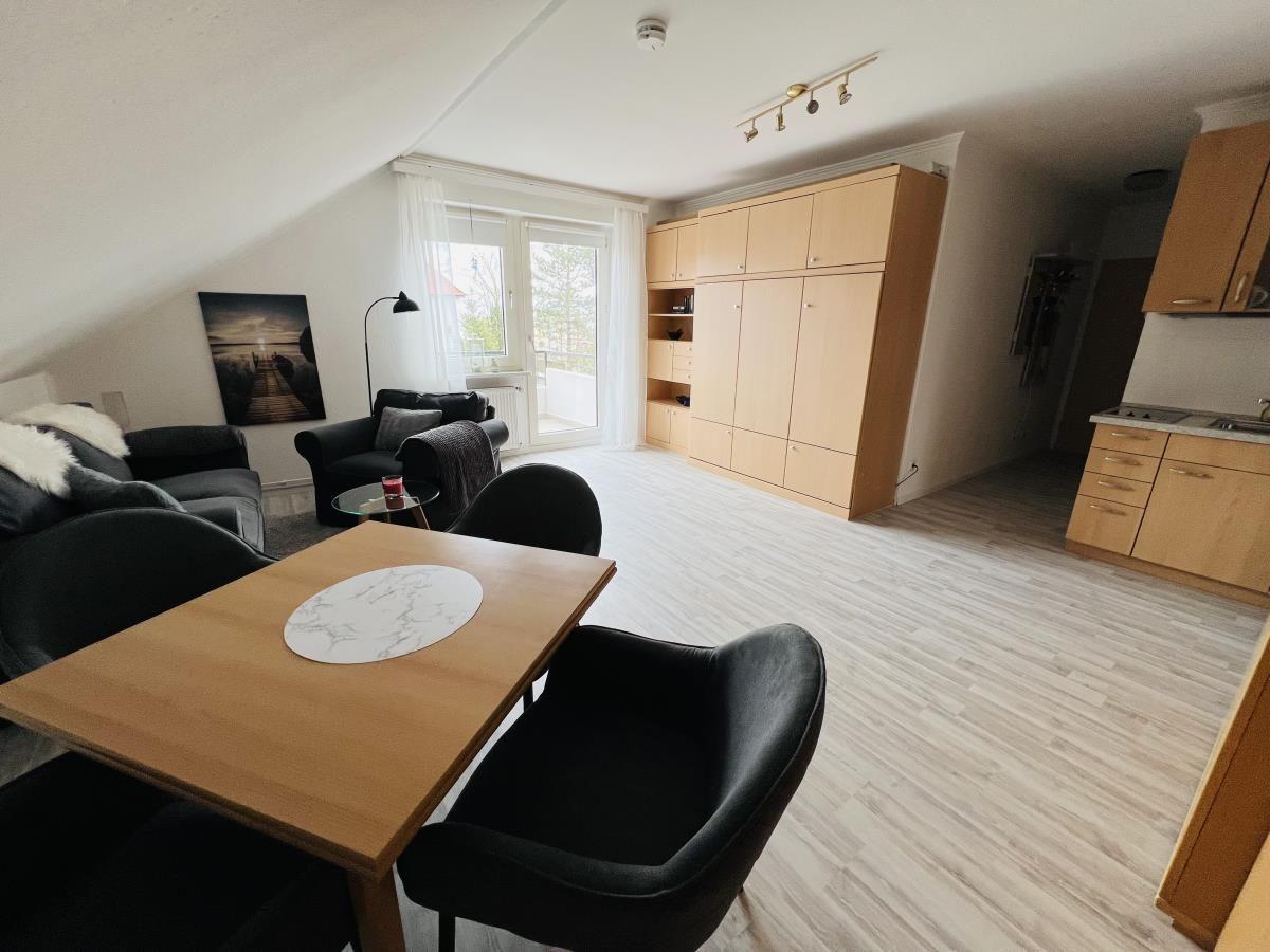 Wohn- und Essbereich mit Küchenzeile und Schlafzimmer im Hintergrund.