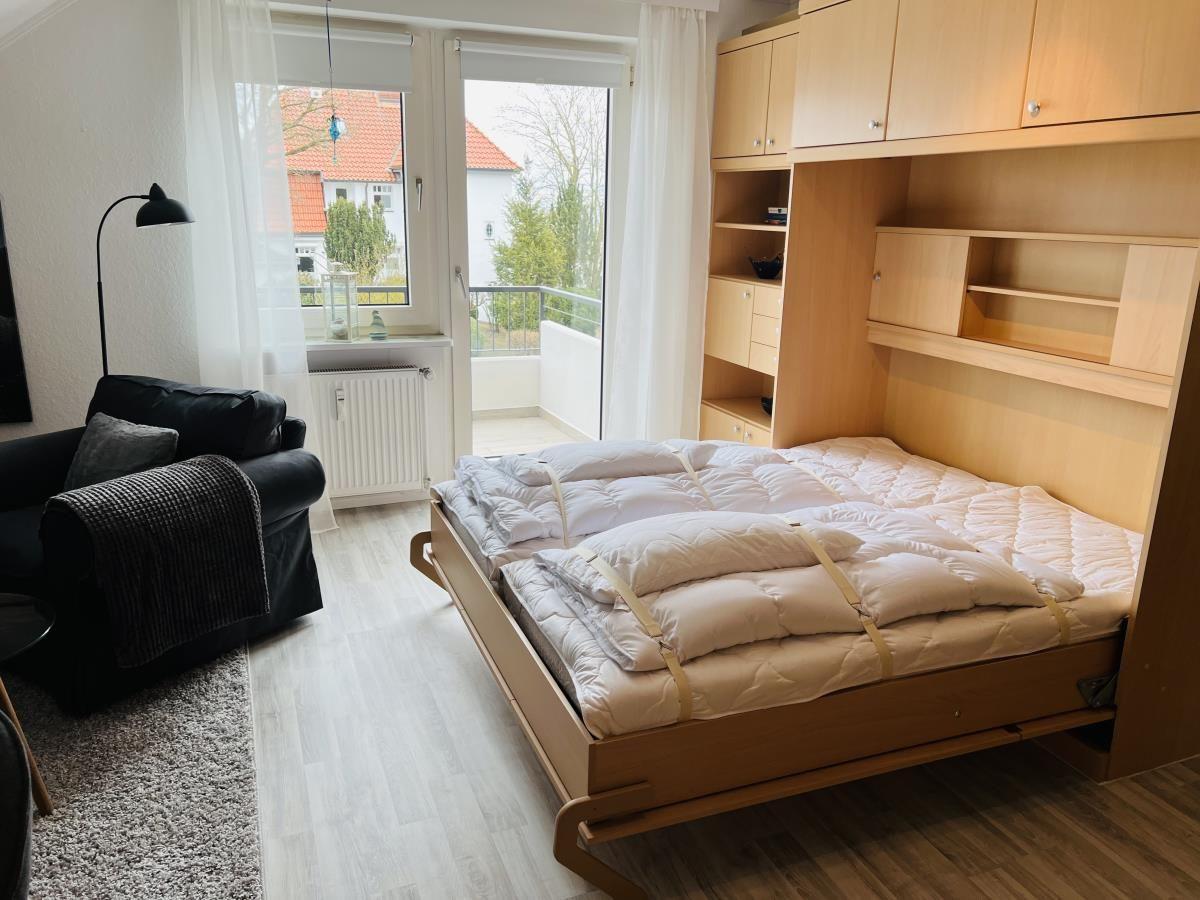 Schlafzimmer mit ausziehbarer Matratze und integriertem Schrank. Fenster mit Blick auf Balkon.