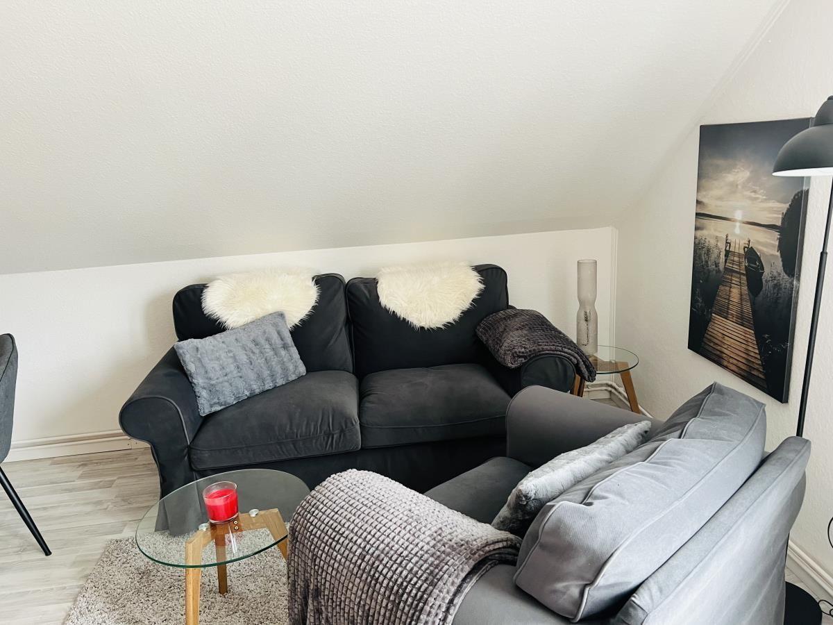 Schwarzes Sofa mit Fellkissen und graue Sitzgelegenheit mit Decke.