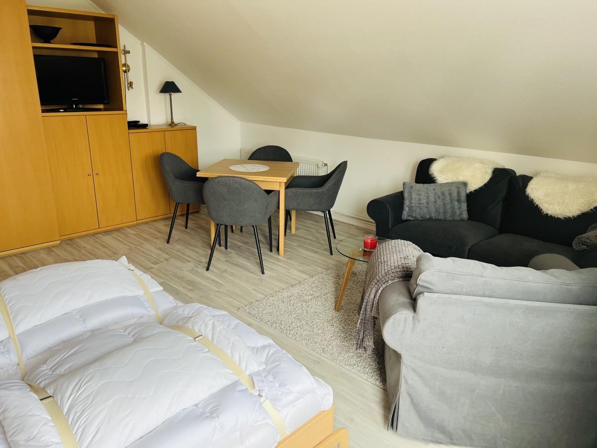 Wohnzimmer mit Sofa, Esstisch und Bett unter Dachschrägen.