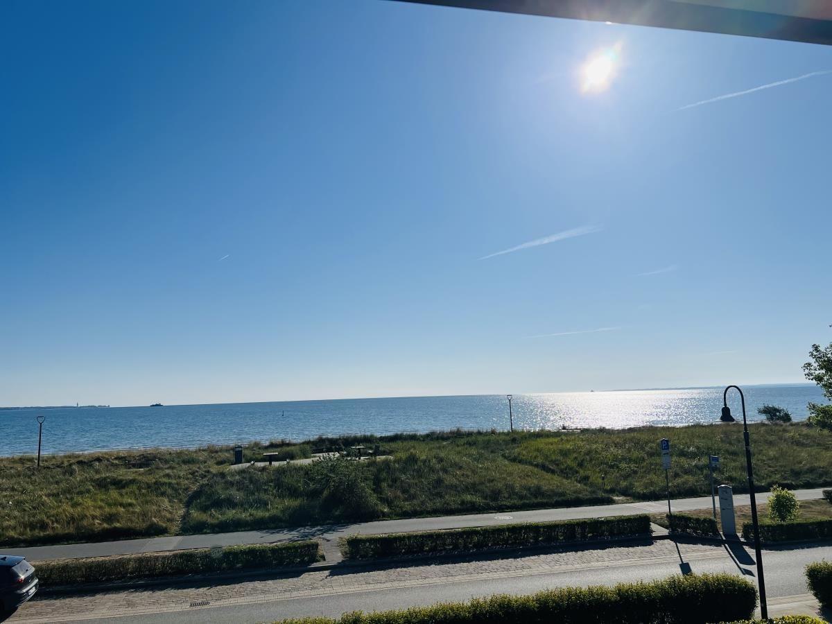 Meeransicht mit Sonne, Strandpromenade und Grünflächen.