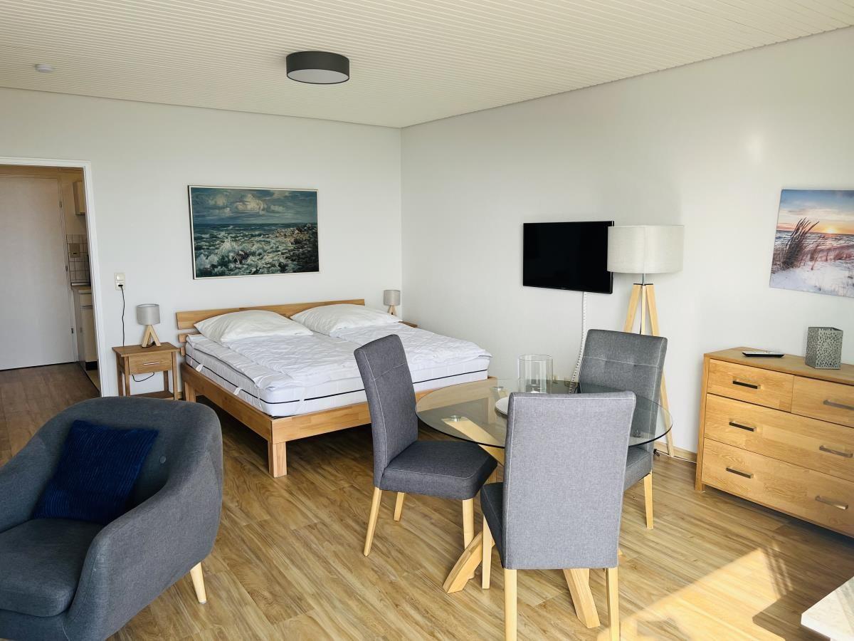 Schlafzimmer mit Bett, Esstisch und Fernseher. Holzboden und Wandbilder.