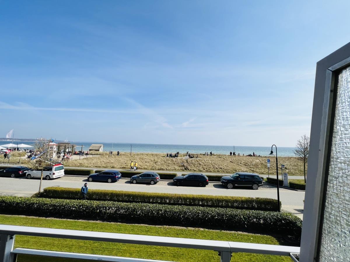 Blick auf Strand mit Parkplatz und Grünflächen unter blauem Himmel.