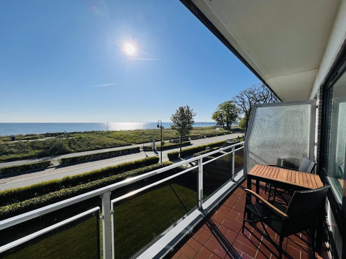 Terrasse mit Tisch und Stühlen, Blick auf Meer und Strandpromenade.