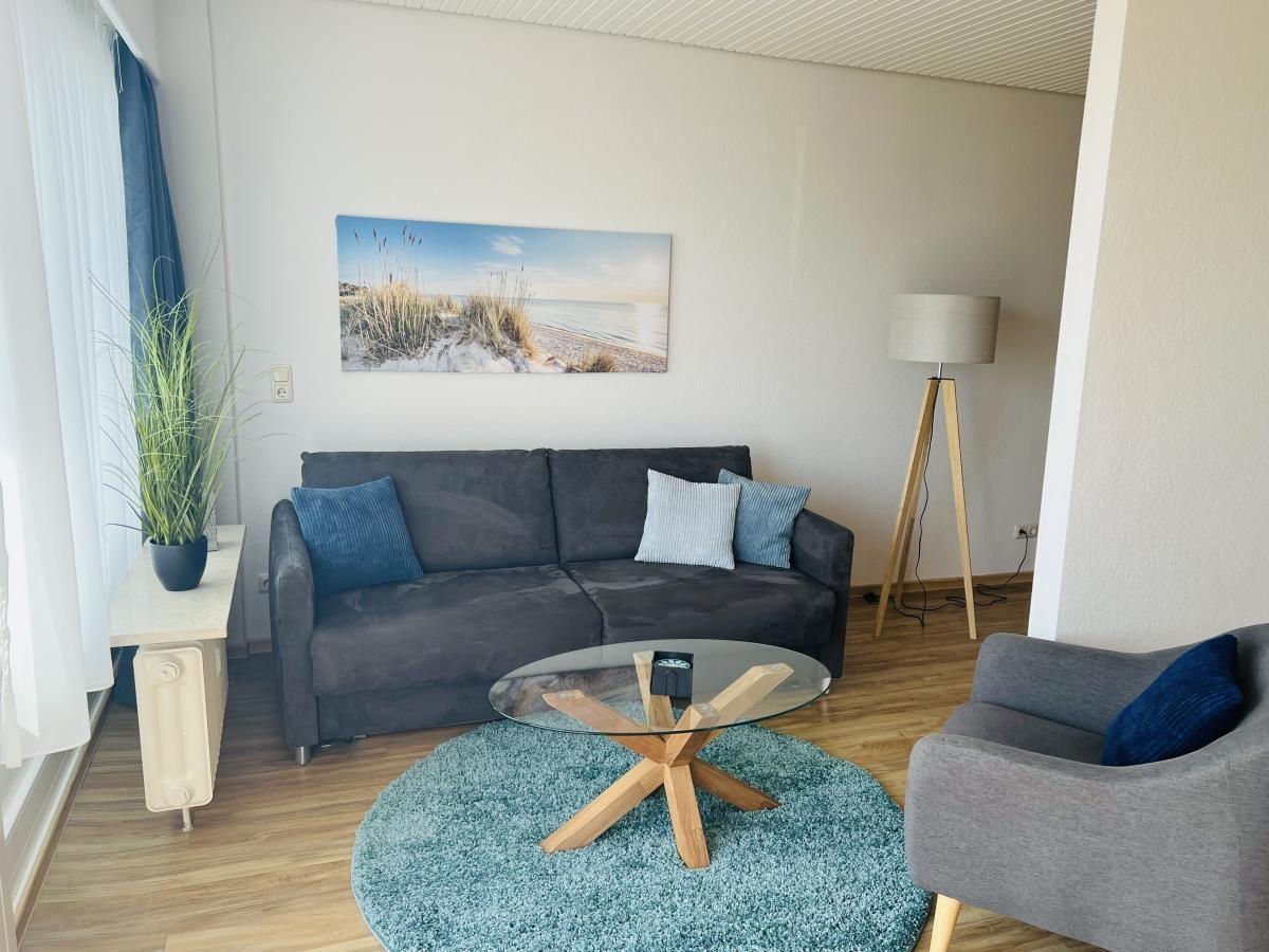 Wohnzimmer mit Sofa, Sessel, Glas-Tisch und Wandbild.