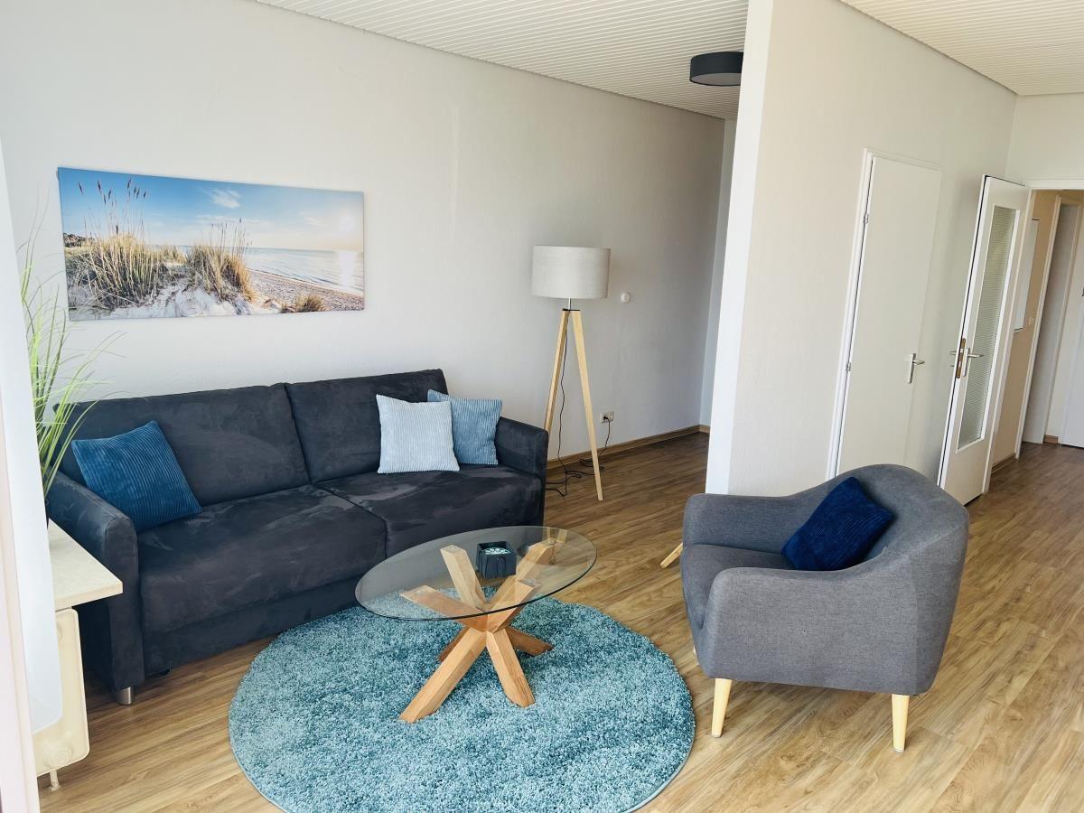 Wohnzimmer mit Sofa, Sessel und Glas-Tisch auf blauem Teppich