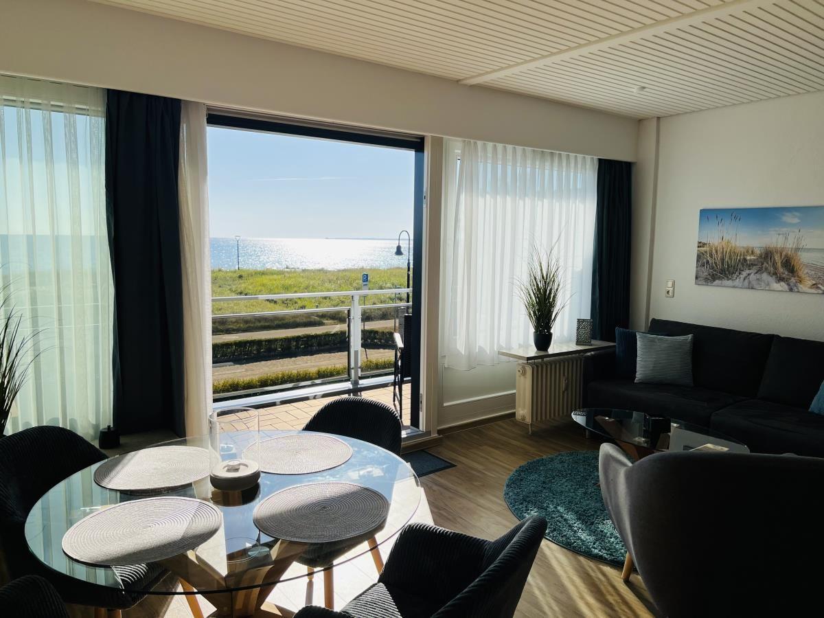 Wohn- und Essbereich mit Meerblick über Balkon. Schwarze Sofas, runder Tisch.