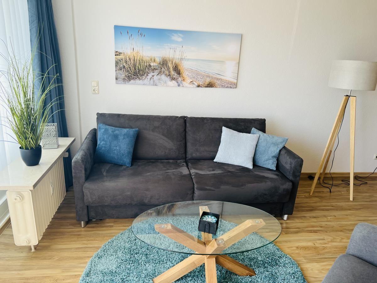 Ein Wohnzimmer mit grauem Sofa, Glas-Tisch und Wandbild.