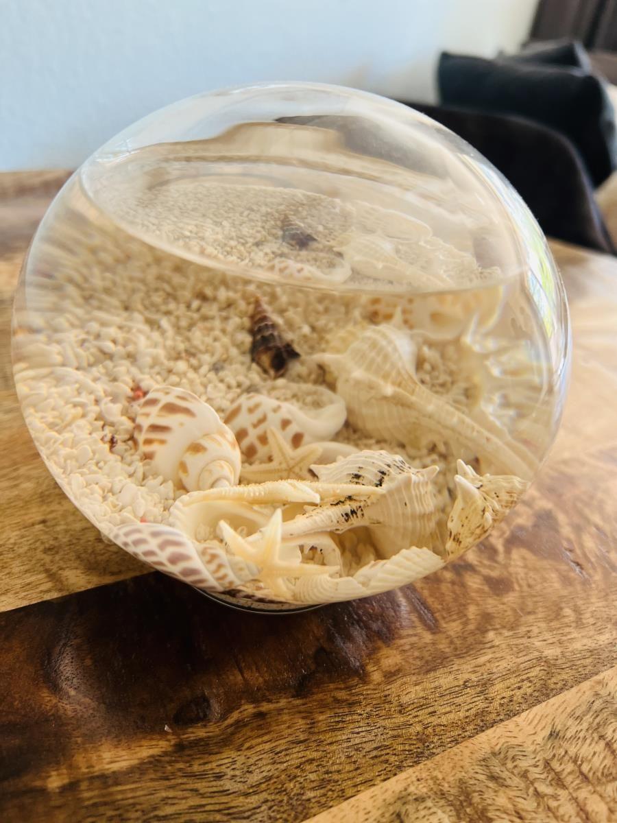 Glasballon mit Sand und Muscheln auf Holztisch