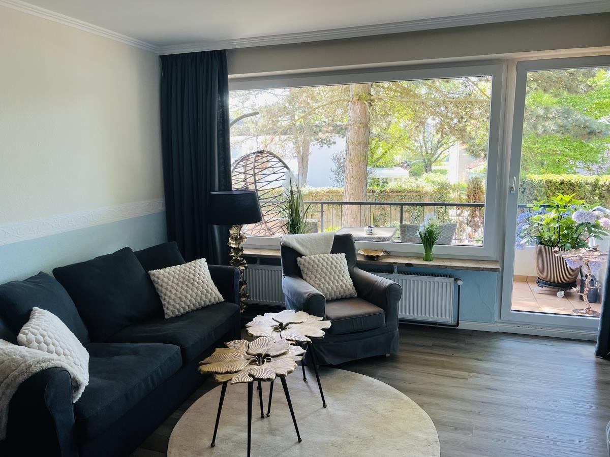 Wohnzimmer mit Sofa, Sessel und Blick auf Balkon mit Pflanzen.