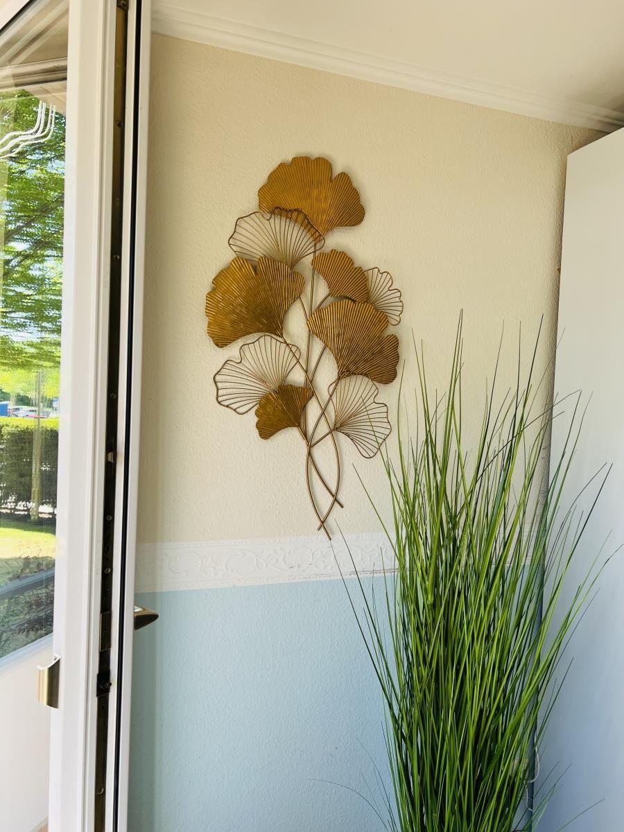 Wanddekoration mit goldfarbenen Blättern und Pflanze in einem Raum mit zweifarbigem Wandverputz.