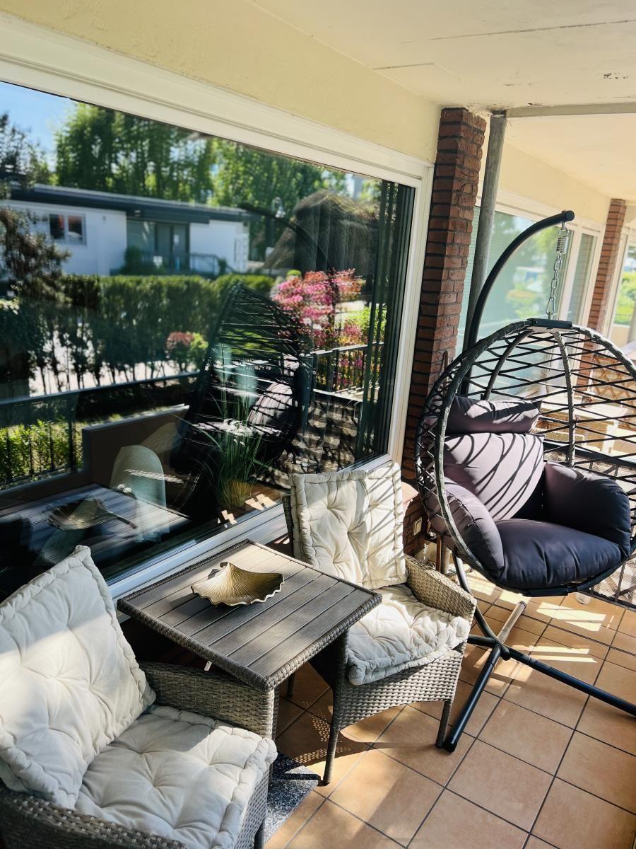 Terrasse mit Hängesessel, Sitzgruppe und Tisch. Blick auf grüne Umgebung.