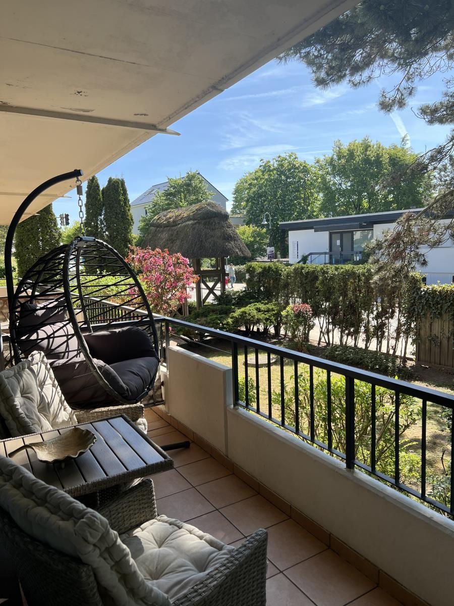 Terrasse mit Hängesessel, Tisch und Stühlen. Blick auf grünen Garten und Häuser.