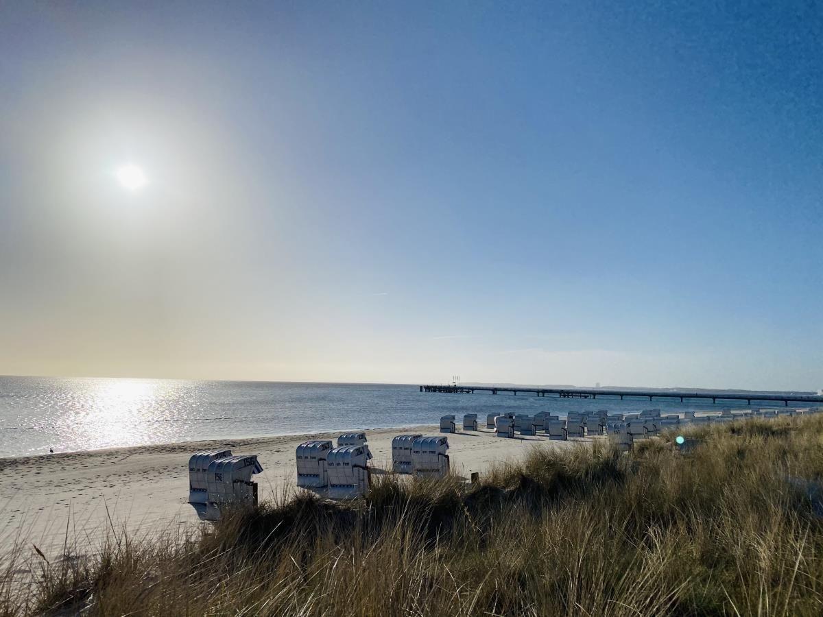 Strand mit Strandkörben und Steg unter blauem Himmel