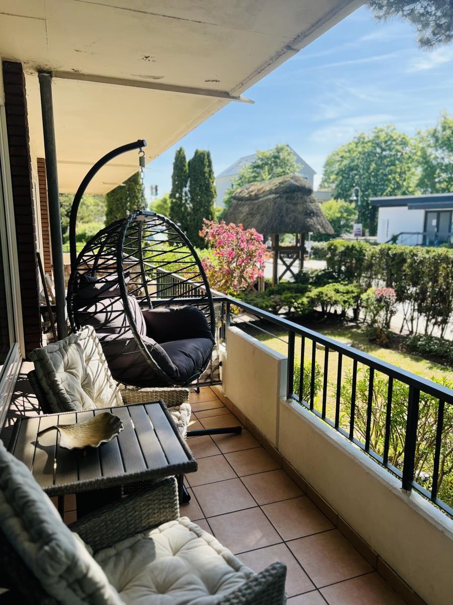 Terrasse mit Hängesessel, Tisch und Stühlen. Blick auf grünen Garten mit Hütte.