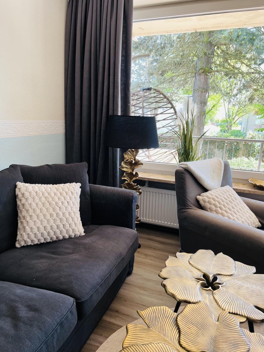 Wohnzimmer mit Sofa, Sessel und Tisch. Blick auf Balkon mit Pflanzen.