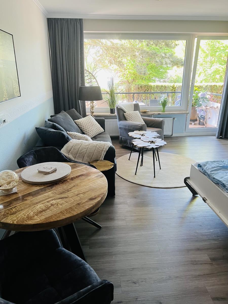 Wohnbereich mit Sofa, Sessel, Tisch und Balkonansicht.