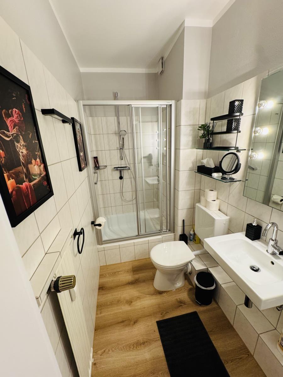 Badezimmer mit Dusche, Toilette und Waschbecken. Holzfußboden und Wandfliesen.