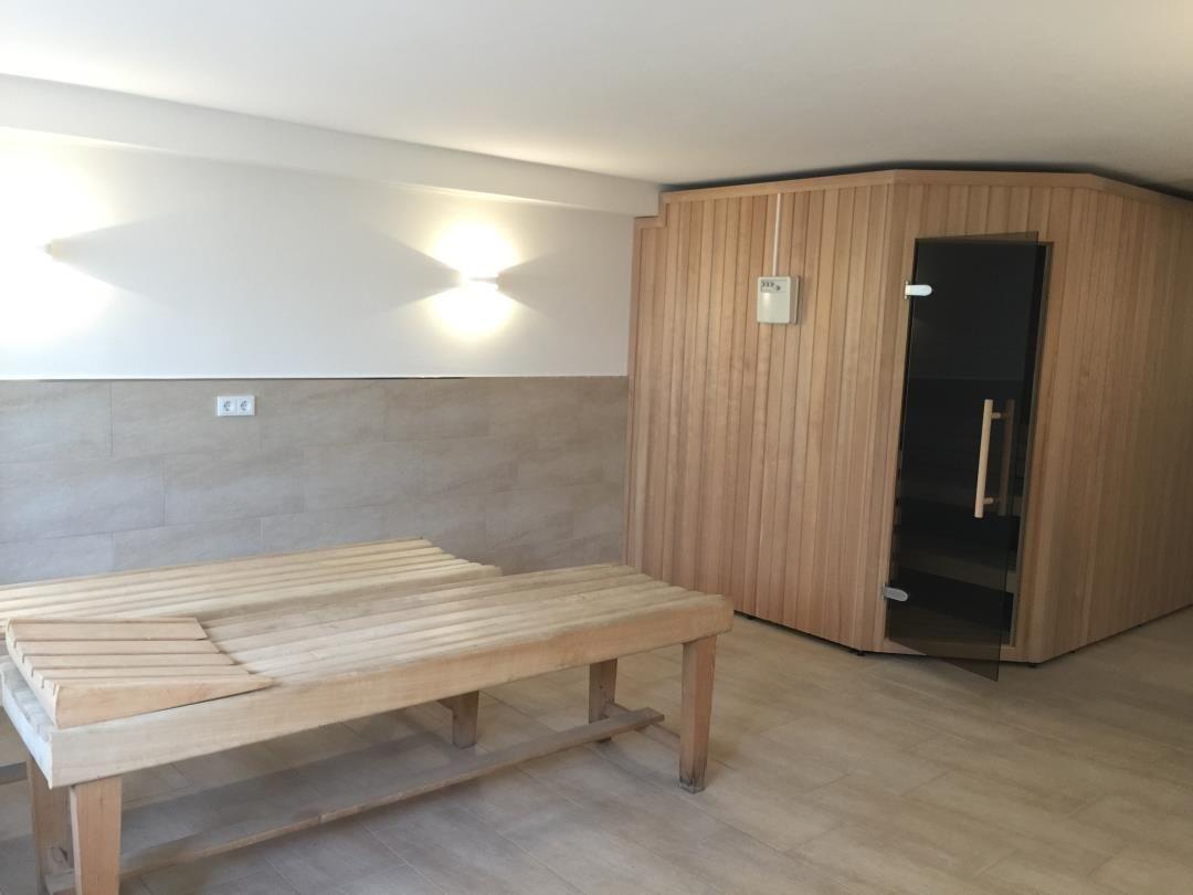 Sauna mit Holzbank und Tür. Wand mit Steinen und Licht.
