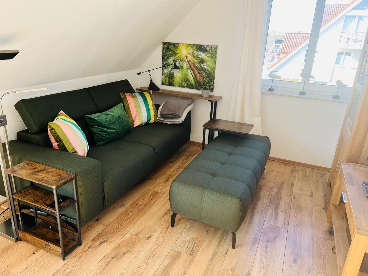 Ein Wohnzimmer mit grünem Sofa, Holzboden und großem Fenster.