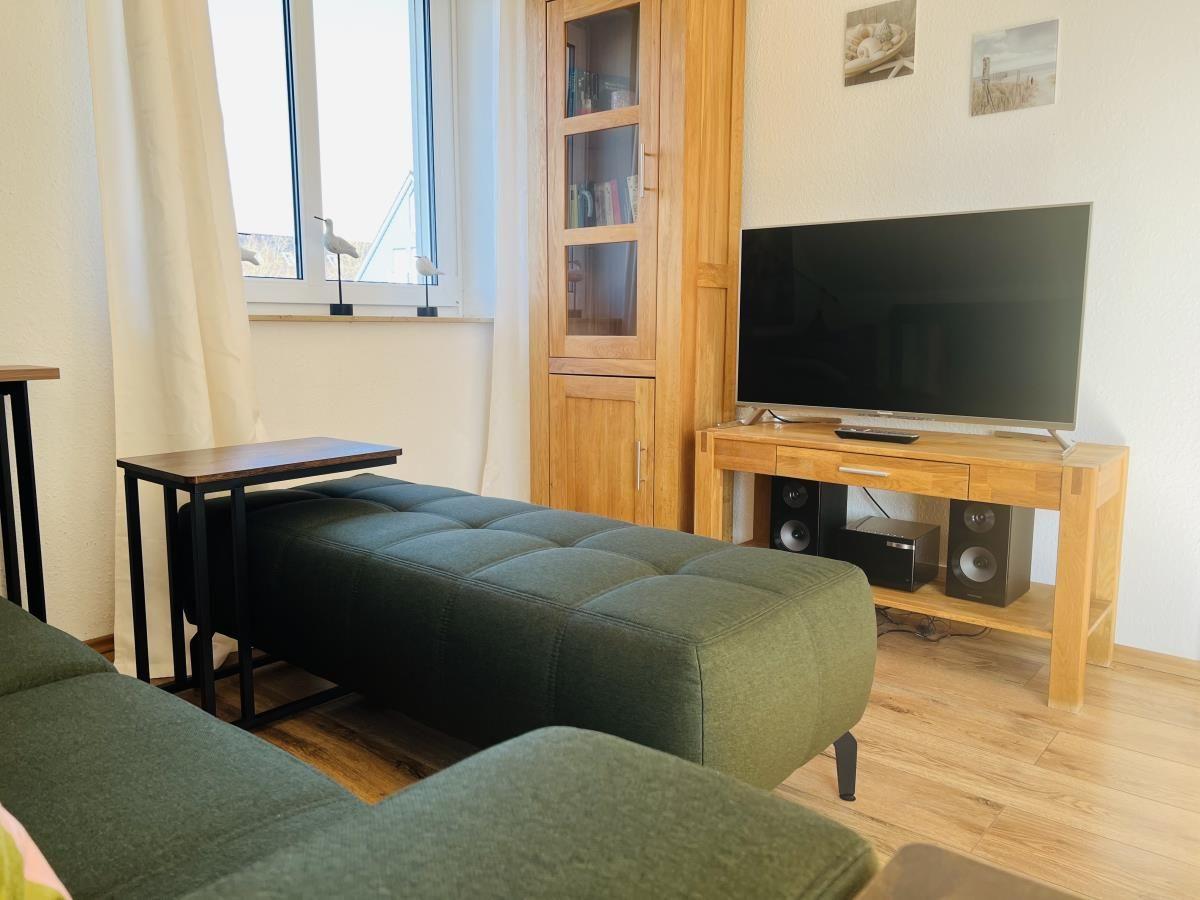Ein Wohnzimmer mit grünem Sofa, Fernseher und Holzmöbeln.