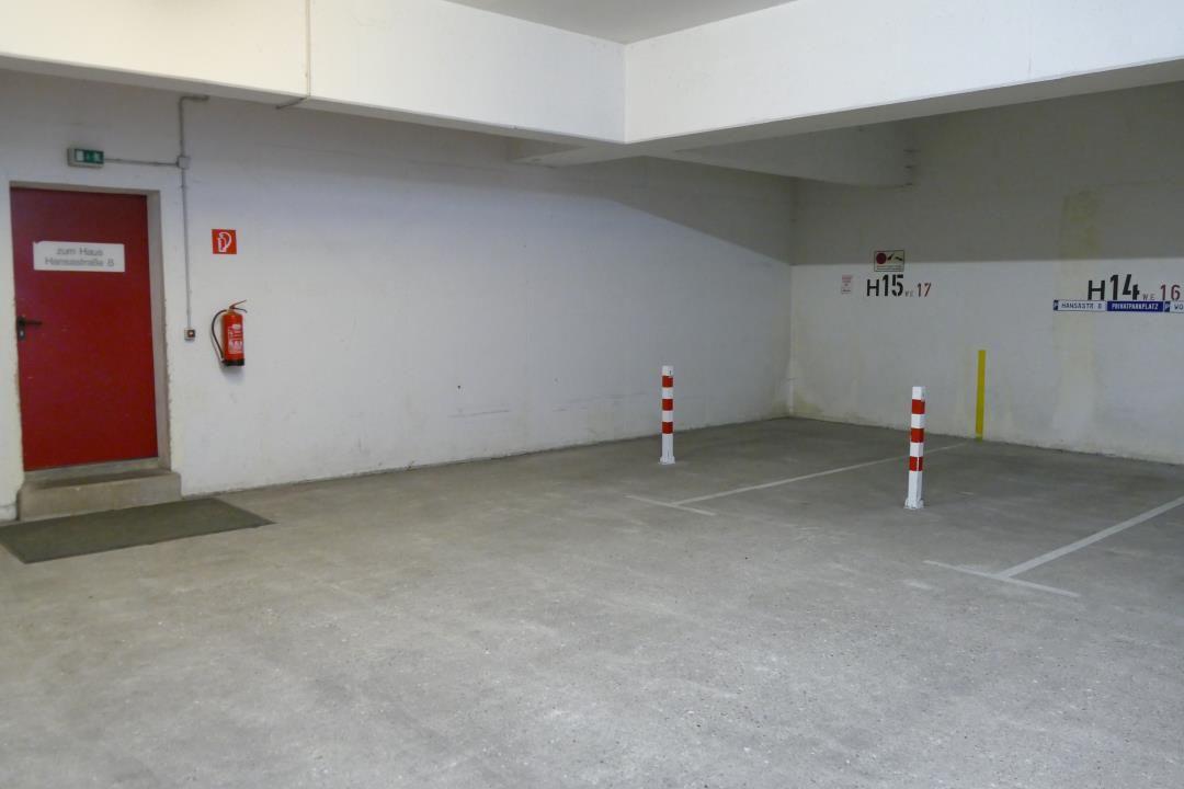 Untergeschoss-Parkplatz mit roter Tür und Feuerlöscher an der Wand.