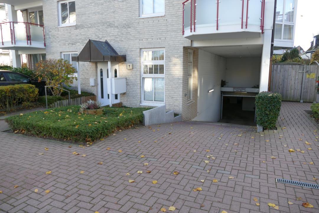 Haus mit Eingang, Garage und gepflasterter Hof mit Hecken und Blumen.