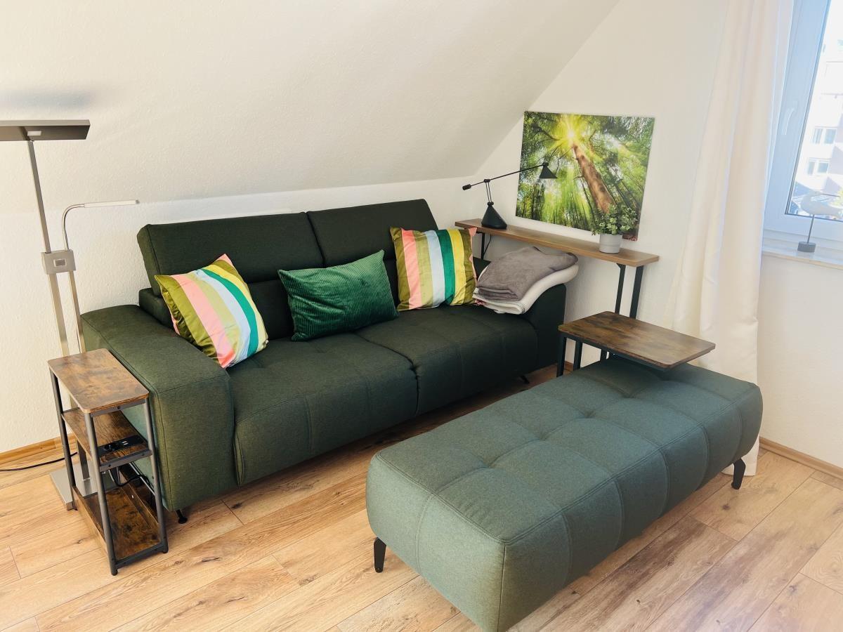 Grünes Sofa mit Kissen, Sitzbank und Tisch im Wohnzimmer mit Holzboden und Fenster.