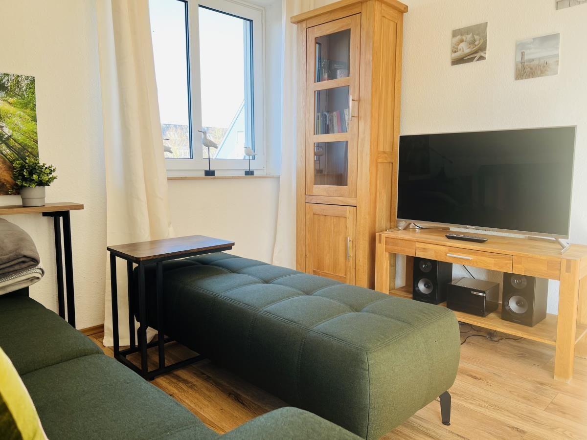 Wohnzimmer mit grünem Sitzbank, Fernseher und Holzmöbeln.