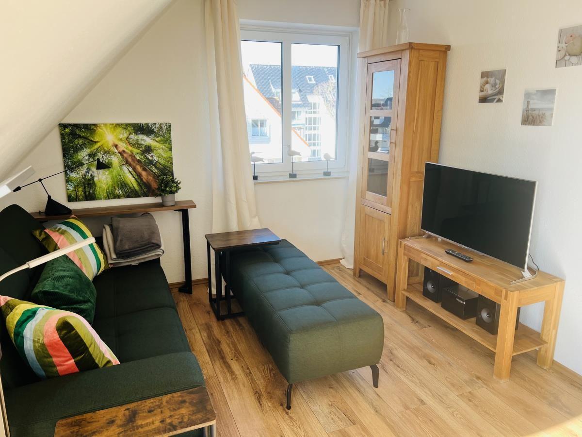 Wohnzimmer mit Sofa, Fernseher und Holzmöbeln. Fenster mit Blick auf Gebäude.